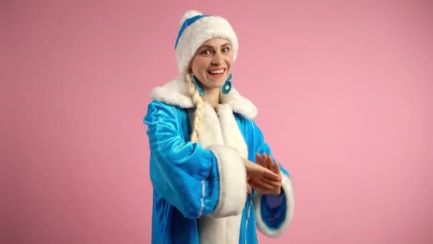 Pembe arka planda dans eden Kar Kızı, mavi Noel kostümlü gülümseyen kadın kameraya bakıyor, elleriyle hareket ediyor ve yavaşça dans ediyor. Noel Baba 'nın geleneksel dansı, Noel tatili. — Stok video