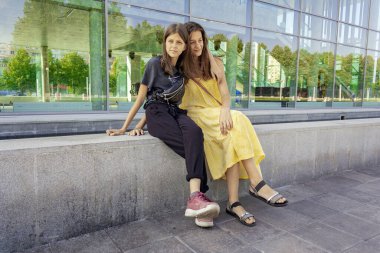 İki kız kardeş şehirde tatil yapıyor. Binanın dışında oturuyorlar. Güneşli bir gün, sıcak bir yorgunluk