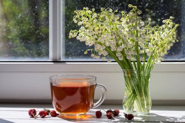 Bir dogrose ve bir buket bahar lilyum vadi üzerinde pencere ile çay.