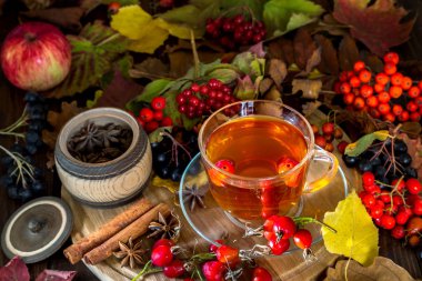 Bir fincan çay sonbahar yaprakları ve meyveleri ahşap arka plan üzerinde arasında.