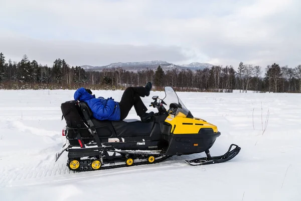 A woman is resting on a snowmobile and admiring the mountains of the Urals.