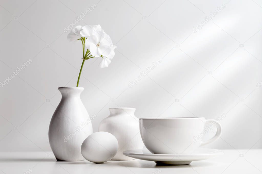 White dishes and a flower in a vase on a light background.
