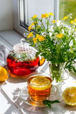 Limonlu ve naneli çay ve güneşli bir günde pencere eşiğinde bir buket çiçek..