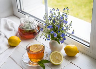 Limonlu ve naneli çay ve güneşli bir günde pencere eşiğinde bir buket çiçek..