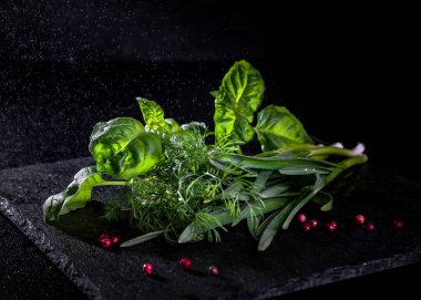 Fesleğen yaprağı, bir demet dereotu ve koyu bir arka planda taze sarımsak..