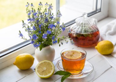 Limonlu ve naneli çay ve güneşli bir günde pencere eşiğinde bir buket çiçek..