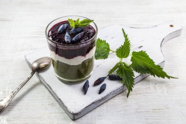 Delicious dessert with a layer of yogurt, smoothie with nettle and honeysuckle. Dessert served in a glass with a spoon. clipart