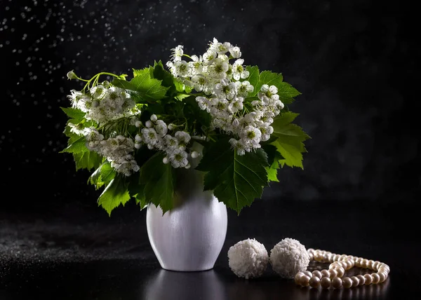 Bouquet of hawthorn, sweets and pearls on a dark background.