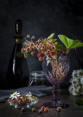 Karanlık bir arka planda, bardakta bir buket orman çileği..