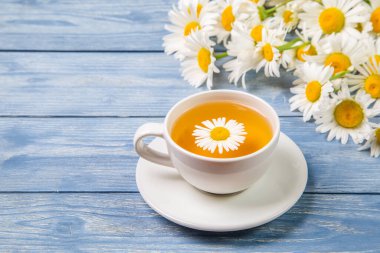 Papatya çiçeklerinden bitki çayı ve mavi arka planda bir buket papatya. Sağlıklı çay kavramı.