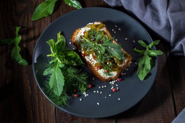 Kaymak peynirli tost, kızarmış sarımsaklı oklar ve koyu bir arka planda otlar..