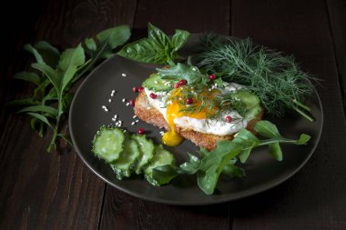 Yumurtalı tost, salatalık ve karanlık bir arka planda otlar..