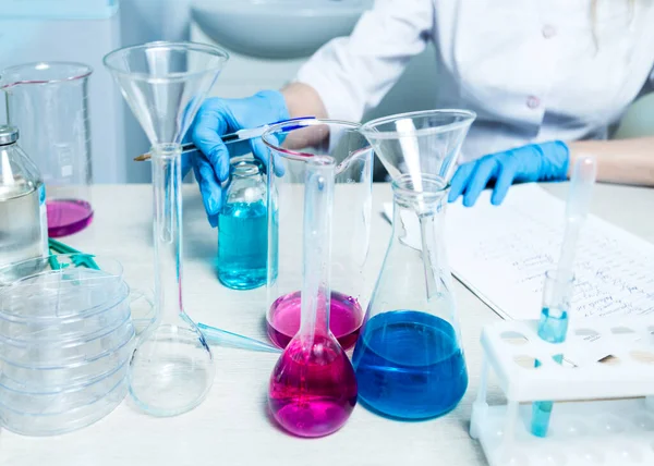 A scientist or doctor in a lab coat writes test results. Laboratory glassware, available chemical fluid.