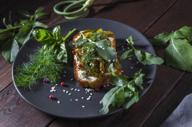 Kaymak peynirli tost, kızarmış sarımsaklı oklar ve koyu bir arka planda otlar..