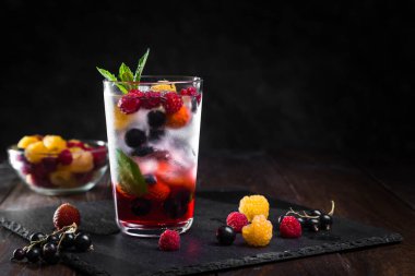 Siyah arka planda şeffaf bir bardakta çilekli limonata..