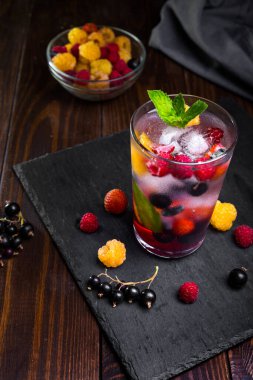 Siyah arka planda şeffaf bir bardakta çilekli limonata..