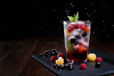 Siyah arka planda şeffaf bir bardakta çilekli limonata..