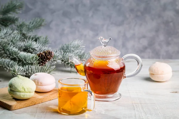 Hot tea with lemon in a transparent bowl and marshmallows on a light background.