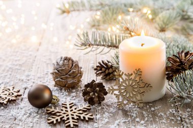 Kırsal ahşap tahtalardaki beyaz Noel mumu - doğal elementler, dallar, çam kozalakları ve Noel süslemeleri ile süslenmiş.