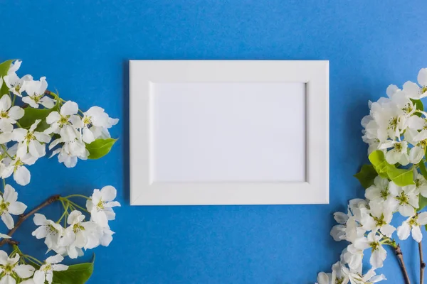 Mockup with a white frame and white spring flowers on a blue background