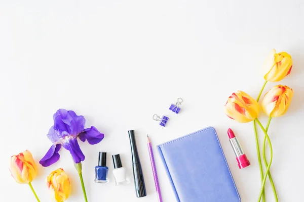 Flat lay blogger or freelancer workspace with a notebook, yellow tulips and blue irises on a white background