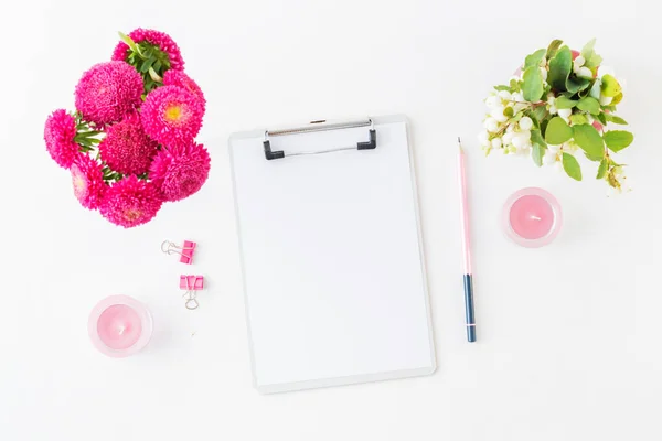 Flat lay blogger or freelancer workspace with a mockup clipboard and pink flowers on a white background