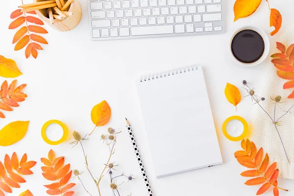 Flat lay blogger or freelancer workspace with a notebook, keyboard, sweater and colorful autumn leaves on a white background
