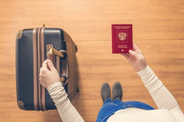 Pasaport kontrolü için havaalanında yürüyen bir bavul ve Rus pasaportu ile bir kızın üst görünümü.