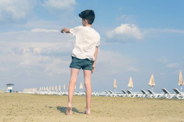 T-shirt ve şort çocuk bulutlu mavi gökyüzü ve iniş uçağı parmağını gösterir. Yaz ve seyahat konsepti