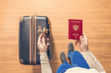 Pasaport kontrolü için havaalanında yürüyen bir bavul ve Rus pasaportu ile bir kızın üst görünümü.