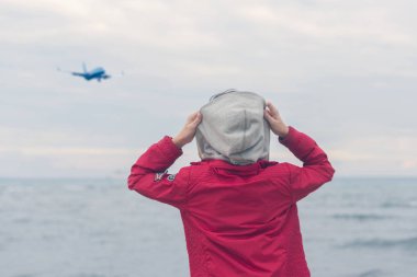 Kırmızı ceketli bir çocuk fırtınalı yağmurlu havalarda deniz dalgalarına bakar. Fırtınalı yağmurlu havalarda deniz dalgaları üzerinde iniş uçağı.