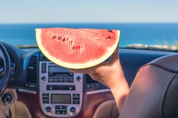 girl traveling by car and holding slice of watermelon.  View from the back seat on the windshield