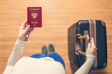 Pasaport kontrolü için havaalanında yürüyen bir bavul ve Rus pasaportu ile bir kızın üst görünümü.