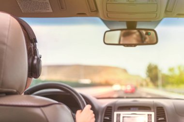 Kulaklıklı kız California'da otobanda araba kullanıyor. Arabanın arka koltuğundan ön cam, yol ve sürücü görünümü