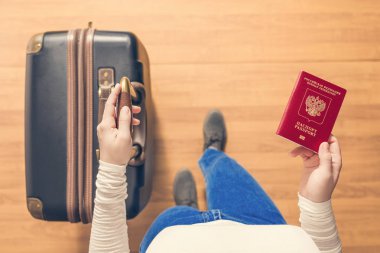 Pasaport kontrolü için havaalanında yürüyen bir bavul ve Rus pasaportu ile bir kızın üst görünümü.