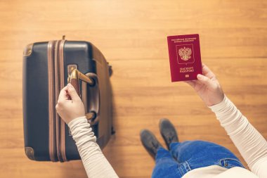 Pasaport kontrolü için havaalanında yürüyen bir bavul ve Rus pasaportu ile bir kızın üst görünümü.