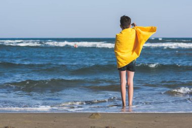 Sahil üzerinde sarı Havlu ayakta çocuğun arka görünümü babasının denizde dalış bekliyor. Aile konsepti.