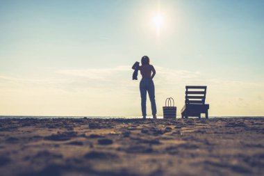 Kadın güneş pansiyonunun yanında duruyor ve çamaşırlarını çıkarıyor. Gün batımında plaj. Yaz konsepti.