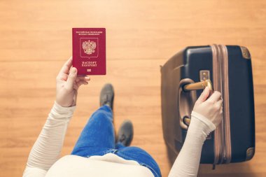 Pasaport kontrolü için havaalanında yürüyen bir bavul ve Rus pasaportu ile bir kızın üst görünümü.