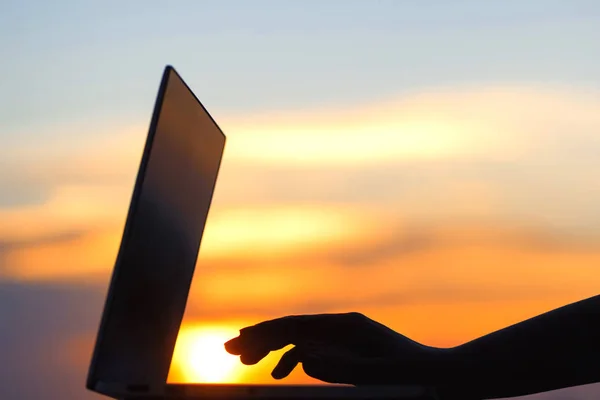 silhouette of a female hand and laptop at sunset at the end of the day. Concept
