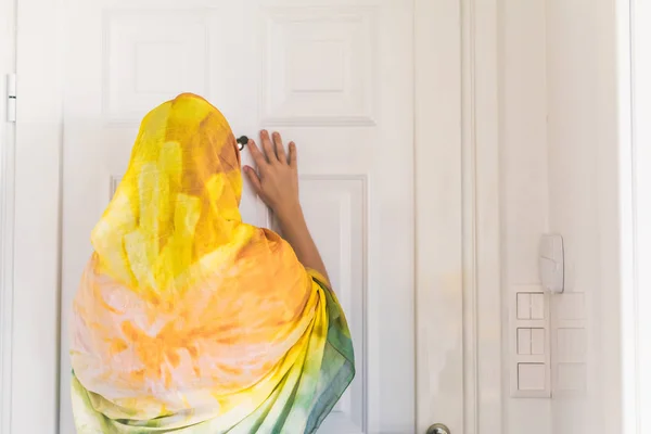 muslim woman in a colorful scarf looking on peephole door when somebody rings the doorbell