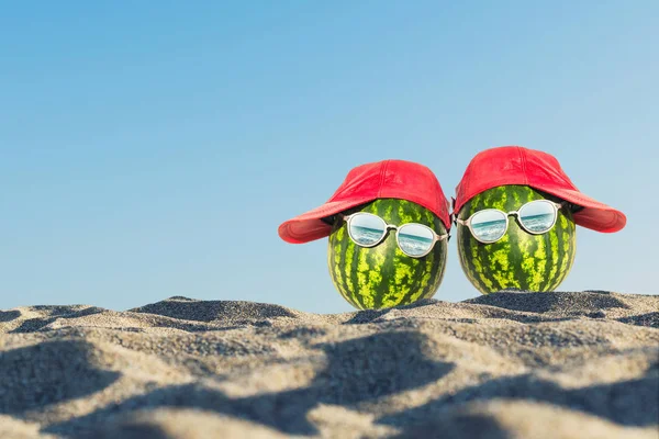 Creative and summer photography of two watermelons in the form of a human head in the glasses in the sand on the beach. Concept
