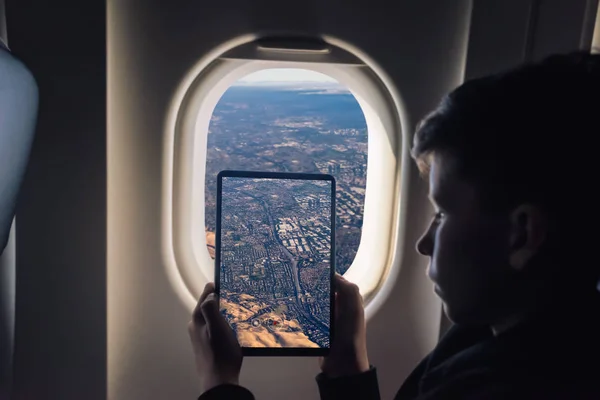 Caucasian boy using tablet pc taking picture through airplane window Redwood Shores State Marine Park and Foster city. San Francisco. California. USA