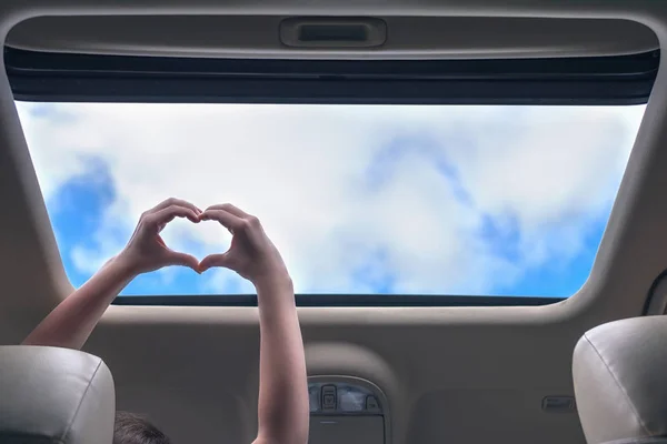 girl traveling by car and holds her hands in the form of heart out from open hatch of a vehicle. Travel lifestyle concept