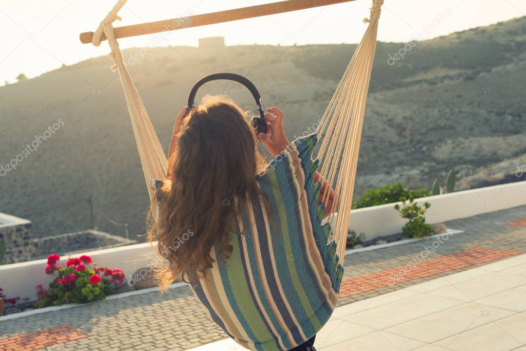 woman with headphones is resting in the Hammack in her villa in the garden at sunset