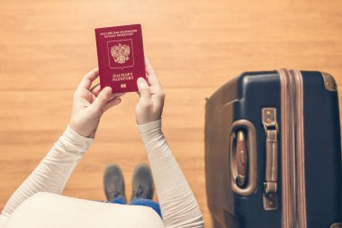 Pasaport kontrolü için havaalanında yürüyen bir bavul ve Rus pasaportu ile bir kızın üst görünümü.