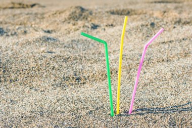 Plastic colored straws tubules for drinking in the sand on the beach. Concept clipart