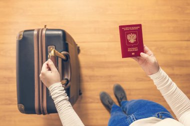 Pasaport kontrolü için havaalanında yürüyen bir bavul ve Rus pasaportu ile bir kızın üst görünümü.