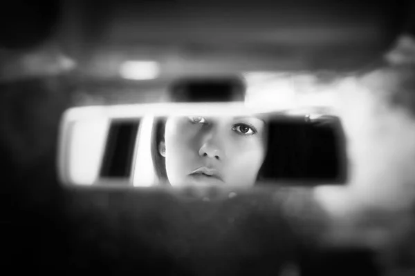 Black and white art picture of beautiful young woman face in the car rear view mirror. concept.