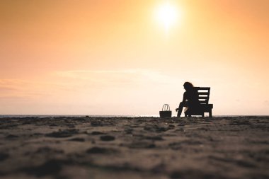 Kız gün batımında sahilde şezlongda oturuyor. Yaz konsepti.